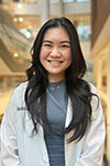 Portrait of Abby Le standing inside wearing a white pharmacist coat and silver necklace