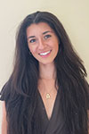 Portrait of Alyssa Toni wearing a black dress and a gold necklace against a beige background
