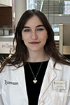 Julia Pollina standing inside in front of a staircase wearing a white coat and silver heart necklace