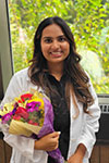 Nimrat Sangha standing in front of a window with trees in the background, holding a colorful bouquet of flowers