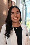 Portrait of Kelly Pham, standing indoors in Pharmacy Hall, wearing a white coat, with large windows in the background